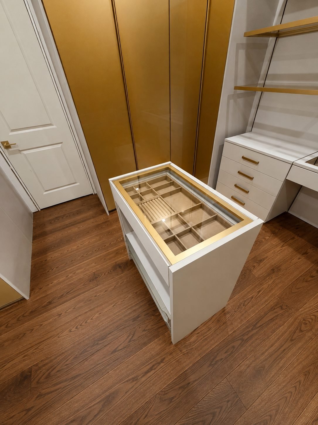 Close view of a jewelry island with glass top and lined compartments in front of a gold lacquer wardrobe