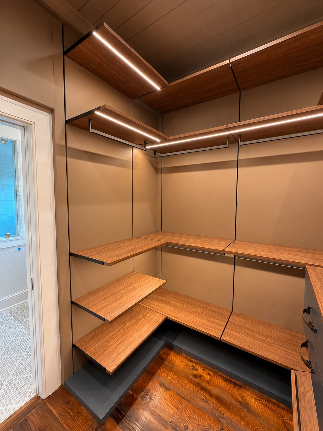 Walnut corner shelving suite with black brackets, linear LED lighting and a doorway opening to a tiled bathroom