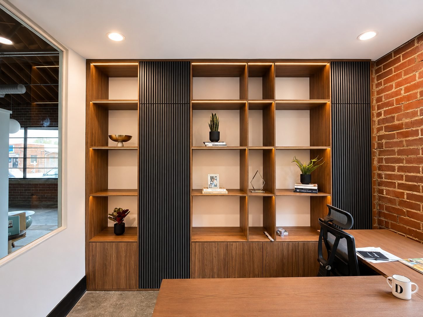 Walnut home office library with illuminated open shelving, black slat panels and an exposed brick accent wall
